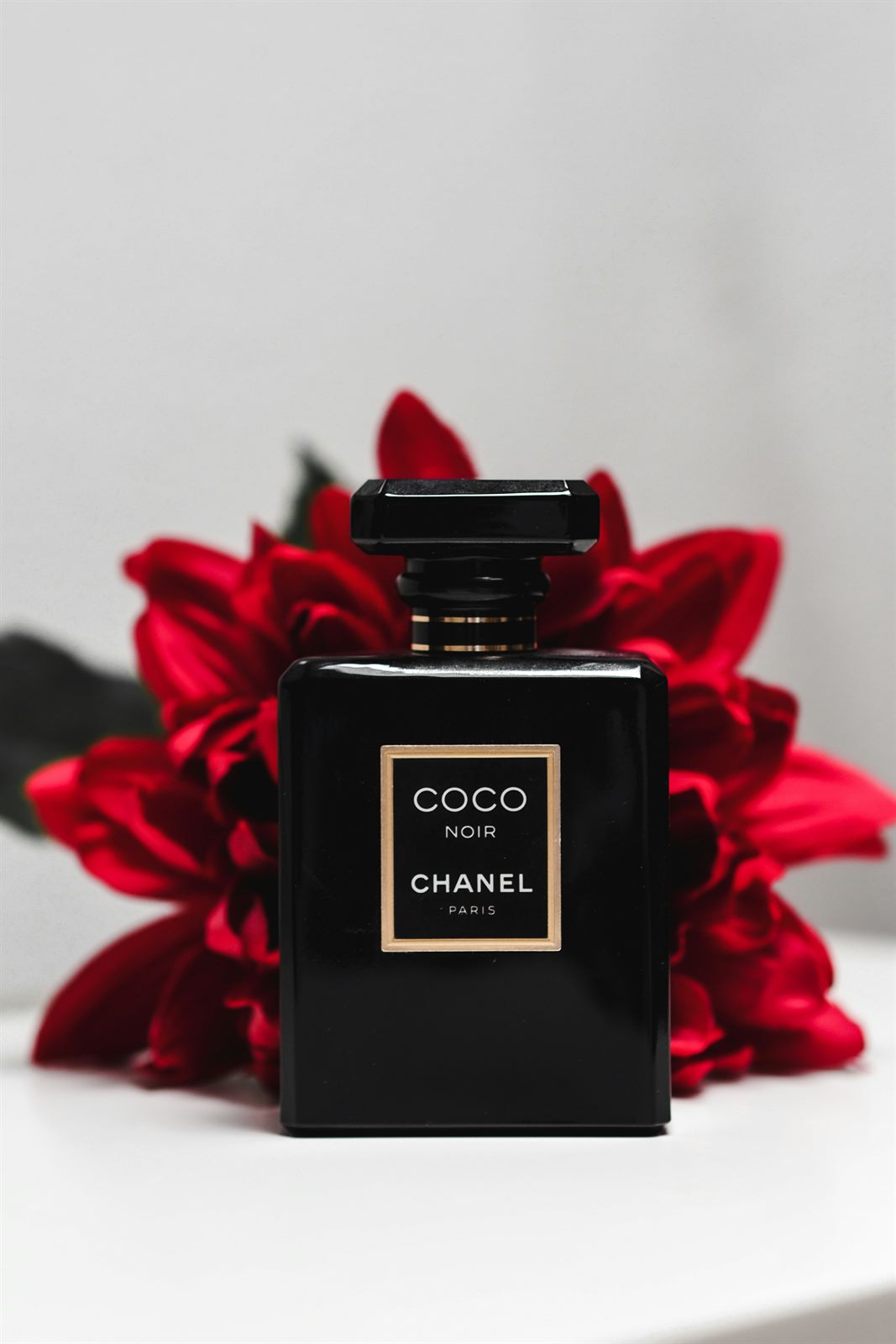 Coco Noir bottle in front of red flowers